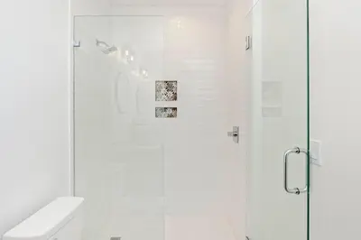 a white bathroom with a shower with a toilet at Ovation- Pool, Beach, Sleeps 21! in Santa Rosa Beach