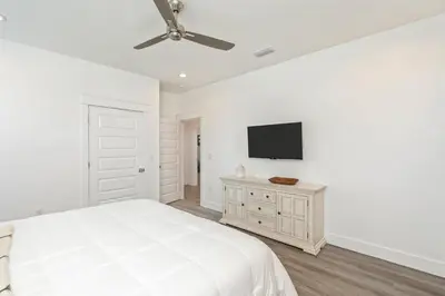 a white bedroom with a bed and a flat screen tv at Ovation- Pool, Beach, Sleeps 21! in Santa Rosa Beach