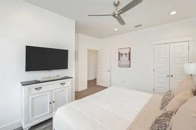 a white bedroom with a bed and a flat screen tv at Ovation- Pool, Beach, Sleeps 21! in Santa Rosa Beach
