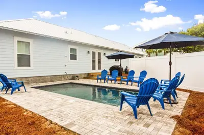 a swimming pool with blue chairs and an umbrella at 4BD3BA Beach House West end PCB in Panama City Beach