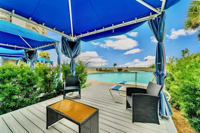 a deck with chairs and an umbrella and a pool at Edgewater Resort! 2BR Sleeps 8! 1st Floor Condo! by Dolce Vita Getaways PCB in Panama City Beach