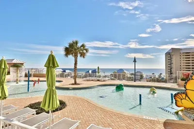 a swimming pool with chairs and umbrellas and the ocean at Sea Turtle at Laketown Wharf in Panama City Beach