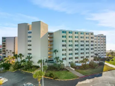 a large white building with palm trees in a parking lot at Beach Front Ocean Front Condo Top of the Gulf 516 in Panama City Beach
