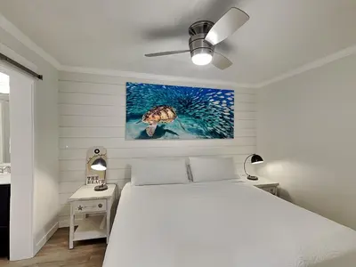a white bedroom with a bed and a turtle painting on the wall at Edgewater Villa #105 in Panama City Beach