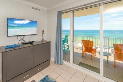 a living room with a television and a balcony at The Sandy Pearl at Ocean Reef in Panama City Beach