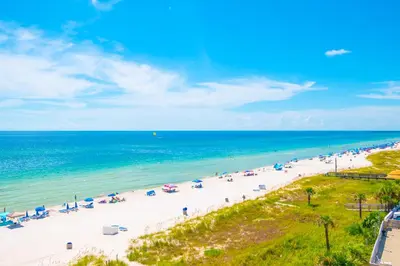 a beach with people and umbrellas and the ocean at The Sandy Pearl at Ocean Reef in Panama City Beach