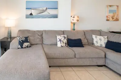 a living room with a gray couch with pillows at The Sandy Pearl at Ocean Reef in Panama City Beach