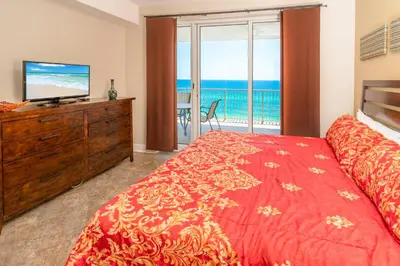 a bedroom with a bed and a television and a balcony at Forever Fun at Ocean Reef in Panama City Beach