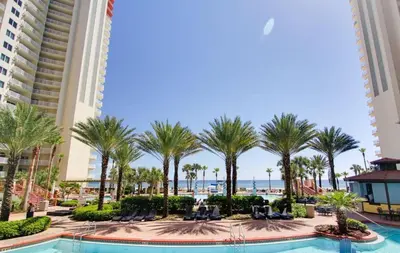 a resort pool with palm trees and the ocean at Pelicans Point South at Shores in Panama City Beach