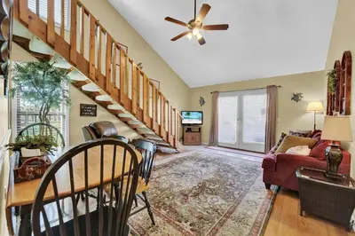 a living room with stairs and a ceiling fan at The Shell House in Panama City Beach