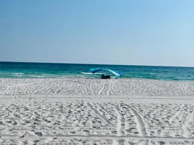 a person sitting on a beach with an umbrella at The Cozy Jamozy in Panama City Beach