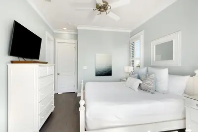 a white bedroom with a white bed and a flat screen tv at Gulf & Lake Views, 6 BR, Pool & 2 minute walk to the beach! in Santa Rosa Beach