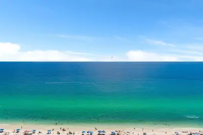 a group of people on a beach with umbrellas at The Summit 1502 - Family Getaway & Beach Chairs in Panama City Beach