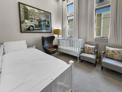 a white bedroom with a crib and two chairs at 224 Winston Ln l 4 Bikes Included l Beachfront with Amazing view l Community Pool in Inlet Beach