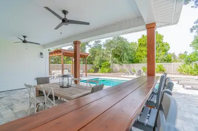 a patio with a wooden table and chairs and a pool at Bid A Wee Bungalow l Outdoor living l Private Pool & Private Beach Access l EV Charging in Panama City Beach