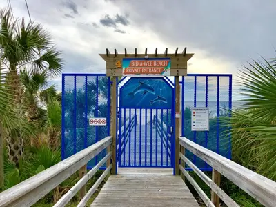 a blue entrance to a beach with a wooden boardwalk at Bid A Wee Bungalow l Outdoor living l Private Pool & Private Beach Access l EV Charging in Panama City Beach