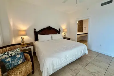 a bedroom with a white bed and a chair at Origins at Seahaven 1504 in Panama City Beach