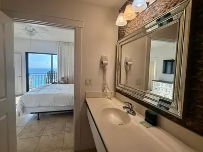 a bathroom with a sink and a mirror and a bed at Origins at Seahaven 1504 in Panama City Beach