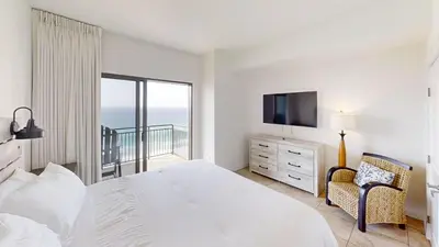 a white bedroom with a bed and a balcony at Origins at Seahaven 1504 in Panama City Beach