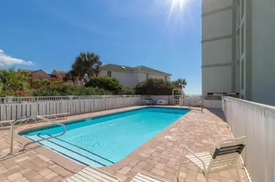 a swimming pool with two chairs next to a building at Commodores 101 l Beachfront l Corner Unit with Pristine Beach Views l Community Pool in Santa Rosa Beach