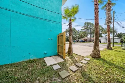 a blue building with a wooden door next to palm trees at Disco Dolphin – Your Funky Beachside Haven in PCB in Panama City Beach