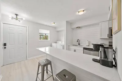 a white kitchen with a counter and a stool at Disco Dolphin Compound | 2x PCB Private Retreats! in Panama City Beach