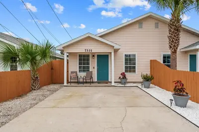 a house with a fence and palm trees at 4 Min Walk to Sand - 2BR - King Bed - Private Yard in Panama City Beach