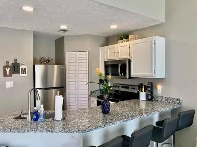 a kitchen with a counter with chairs and a refrigerator at Sunset Dreams - King Bed - 5 Min Walk to Beach in Panama City Beach