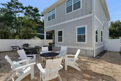 a patio with white chairs and a table and a house at Sunlit Sands in Inlet Beach