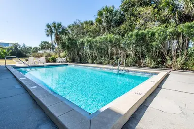 a swimming pool with blue water and trees at Inlet Sands 204 l 1 min walk to beach l Community Pool l Bike to Rosemary in Inlet Beach