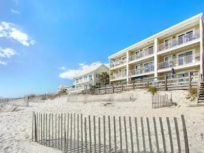 a building on the beach with a fence in front of it at Leeward II 3 l Beachfront Condo l Large first level deck with steps down to sand in Seagrove Beach