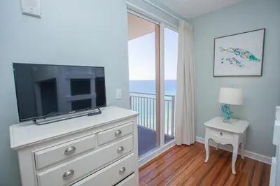 a bedroom with a dresser with a television and a balcony at Splash 1701E - 2BD in Panama City Beach