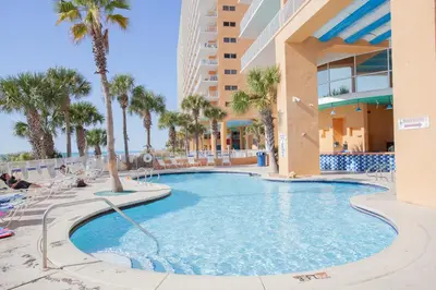 a swimming pool with chairs and palm trees in a resort at Splash 1701E - Studio in Panama City Beach