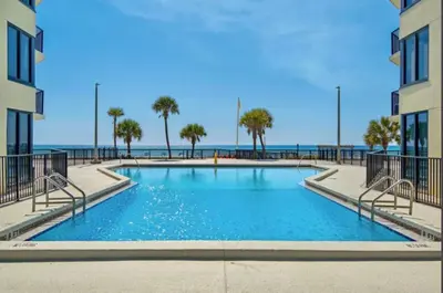 a swimming pool with the ocean in the background at Modern Condo! Free Beach Chairs & Pools by Dolce Vita Getaways PCB in Panama City Beach