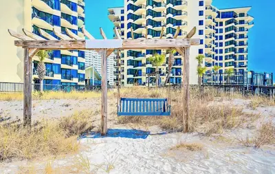 a bench on the beach in front of a building at Modern Condo! Free Beach Chairs & Pools by Dolce Vita Getaways PCB in Panama City Beach