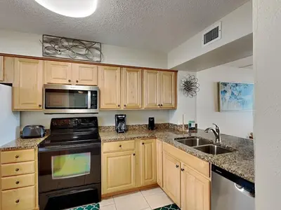 a kitchen with wooden cabinets and a stove and a sink at Dunes of Panama #B301 in Panama City Beach