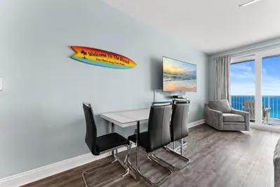 a dining room with a table and chairs and a surfboard on the wall at 3 BD Gulf View Resort Condo! 5 Pools! Beach Access by Dolce Vita Getaways in Panama City Beach