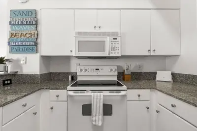 a white kitchen with a stove and a microwave at Shores of Panama Ground Floor Unit 108! No elevators needed and convenient same-floor parking! in Panama City Beach