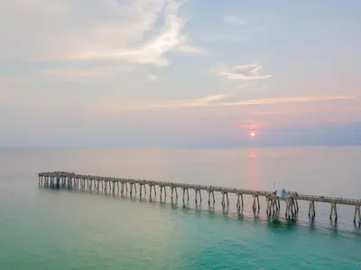 a pier in the ocean with the sun setting at Paradise by the Pier l Ocean Views l Dog Friendly l Steps to Pier Park Shopping and Restaurants in Panama City Beach