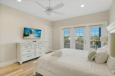 a white bedroom with a bed and a dresser with a tv at Pura Vida l 5 Bedroom l Private Pool l Walk to Beach l Panama City Beach in Panama City Beach