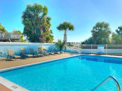 a swimming pool with chairs and palm trees at SummerTowne 1 At Pier Park l Amazing Ocean Views l Dog Friendly l Community Pool in Panama City Beach