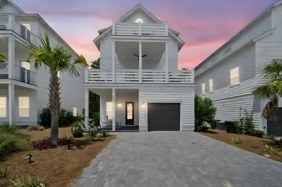 a white house with a garage and a palm tree at The Way of Water l Community Pool l 2 Bikes included in Inlet Beach