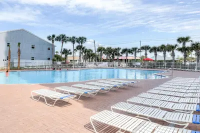 a pool with white lounge chairs in front of a building at Tidewater 311 l Beachfront with pristine views l Heated Pool & Jacuzzi l Gym and Game room and Theatre in Panama City Beach