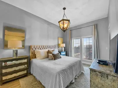 a bedroom with a bed and a television and a chandelier at Twickenham l Heated Community Pool l Private Balcony l Close to Rosemary in Rosemary Beach