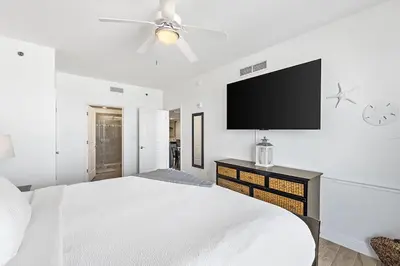 a white bedroom with a bed and a flat screen tv at Sterling Breeze 307B by Emerald Coast Retreats in Panama City Beach