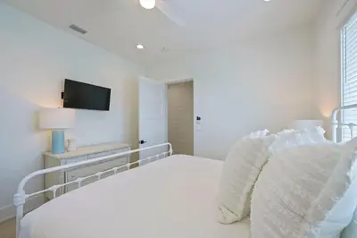 a white bedroom with a bed and a tv on the wall at Big Gus - Huge Home Near the Beach with Gulf Views & Secluded Pool Area in Rosemary Beach