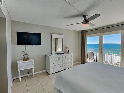 a bedroom with a bed and a television and a balcony at Dunes of Panama #D705 in Panama City Beach