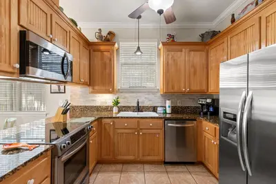 a kitchen with wooden cabinets and a stainless steel refrigerator at Sunset Cove: Charming 3BR/3BA Beach House Sleeps 8 with Sunsets & Serenity in Panama City Beach