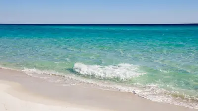 a wave breaking on a beach next to the ocean at Sunset Cove: Charming 3BR/3BA Beach House Sleeps 8 with Sunsets & Serenity in Panama City Beach