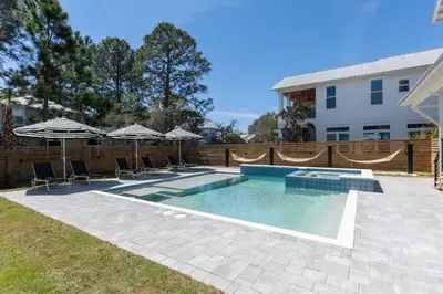 a swimming pool with chairs and umbrellas next to a building at The Gathering Place by Travel Life Vacations in Santa Rosa Beach